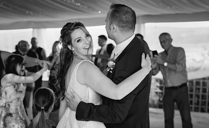 Bride smiling to the camera while dancing with groom