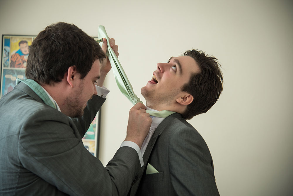 Groomsman pretending to be hung while doing up his tie
