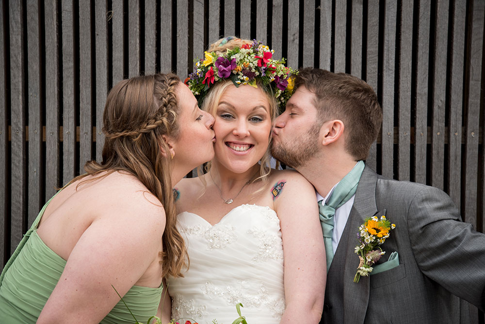 Maid of honour and groom kissing the bride
