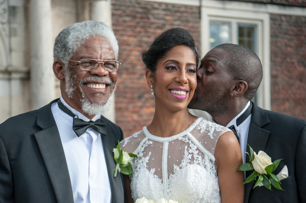 Groom kissing bride&rsquo;s cheek with father of the groom