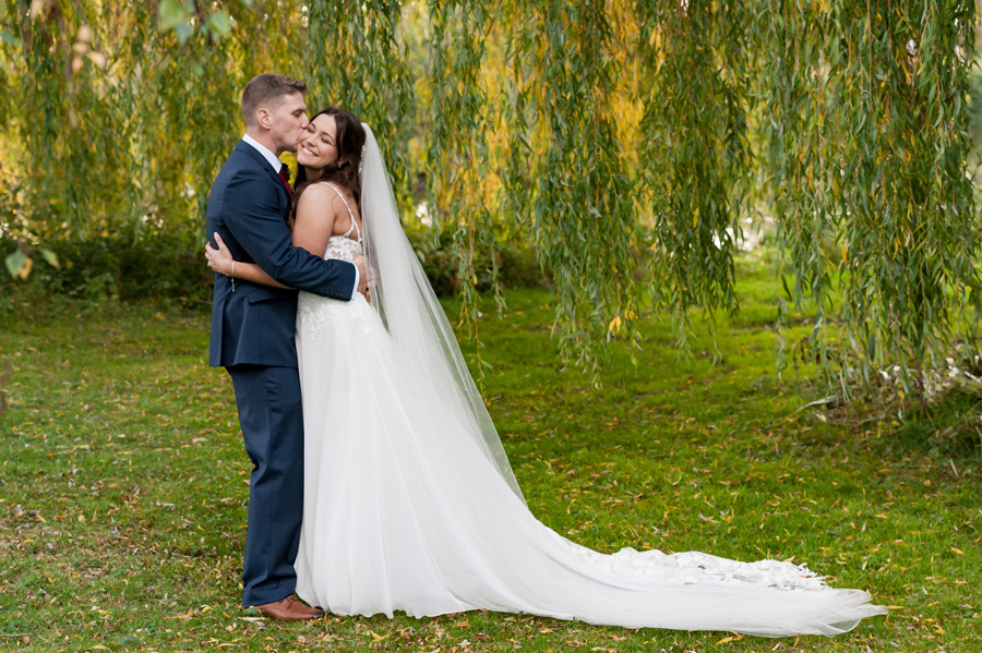 Newlywed couple hugging by willow tree