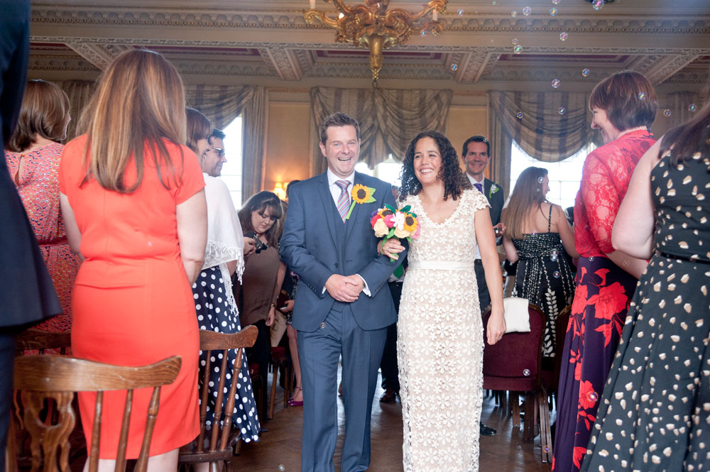 Couple leaving ceremony room while guests blow bubbles