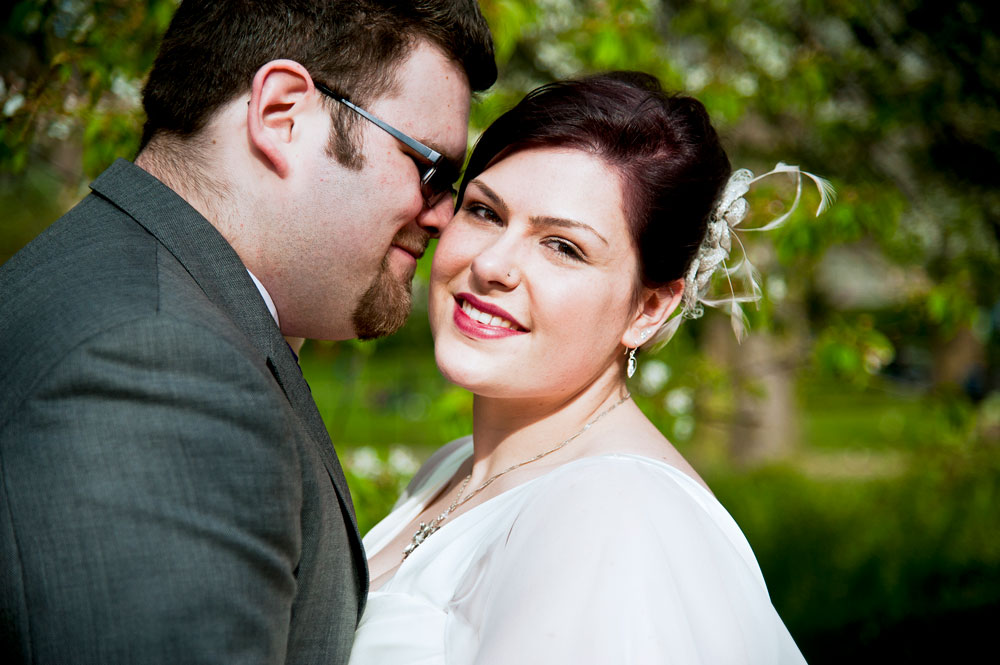 Bride looking to camera while groom kisses her cheek