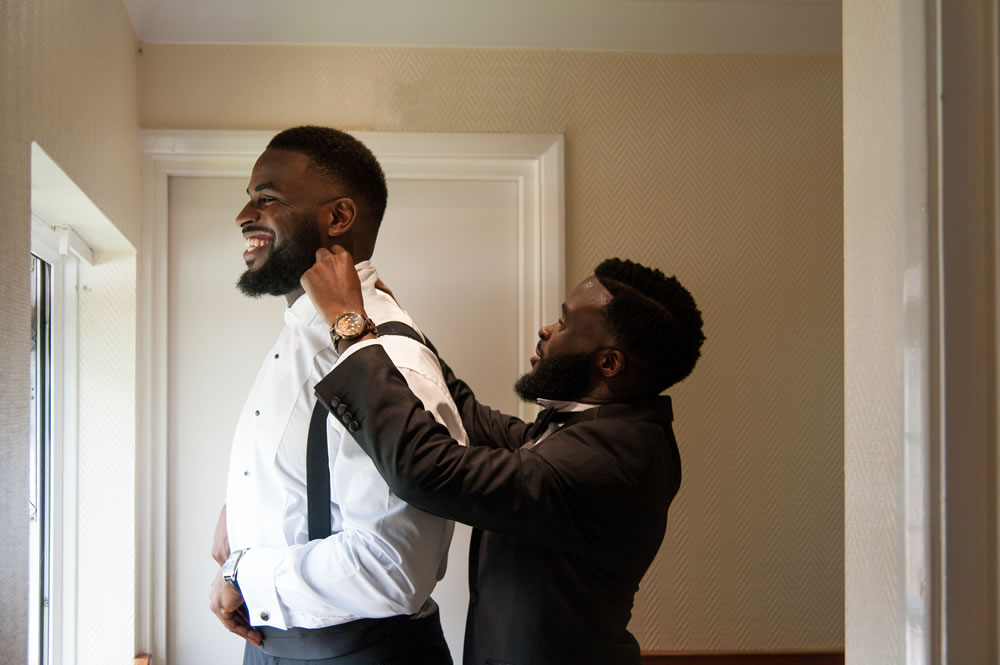 Groomsman fixing groom&rsquo;s collar